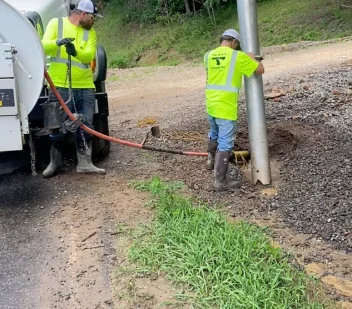 A technician working a hydrovac wand on a gravel shoulder next to the vacuum truck