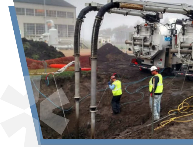 Two operators running hydrovac lances into an excavation at an industrial site